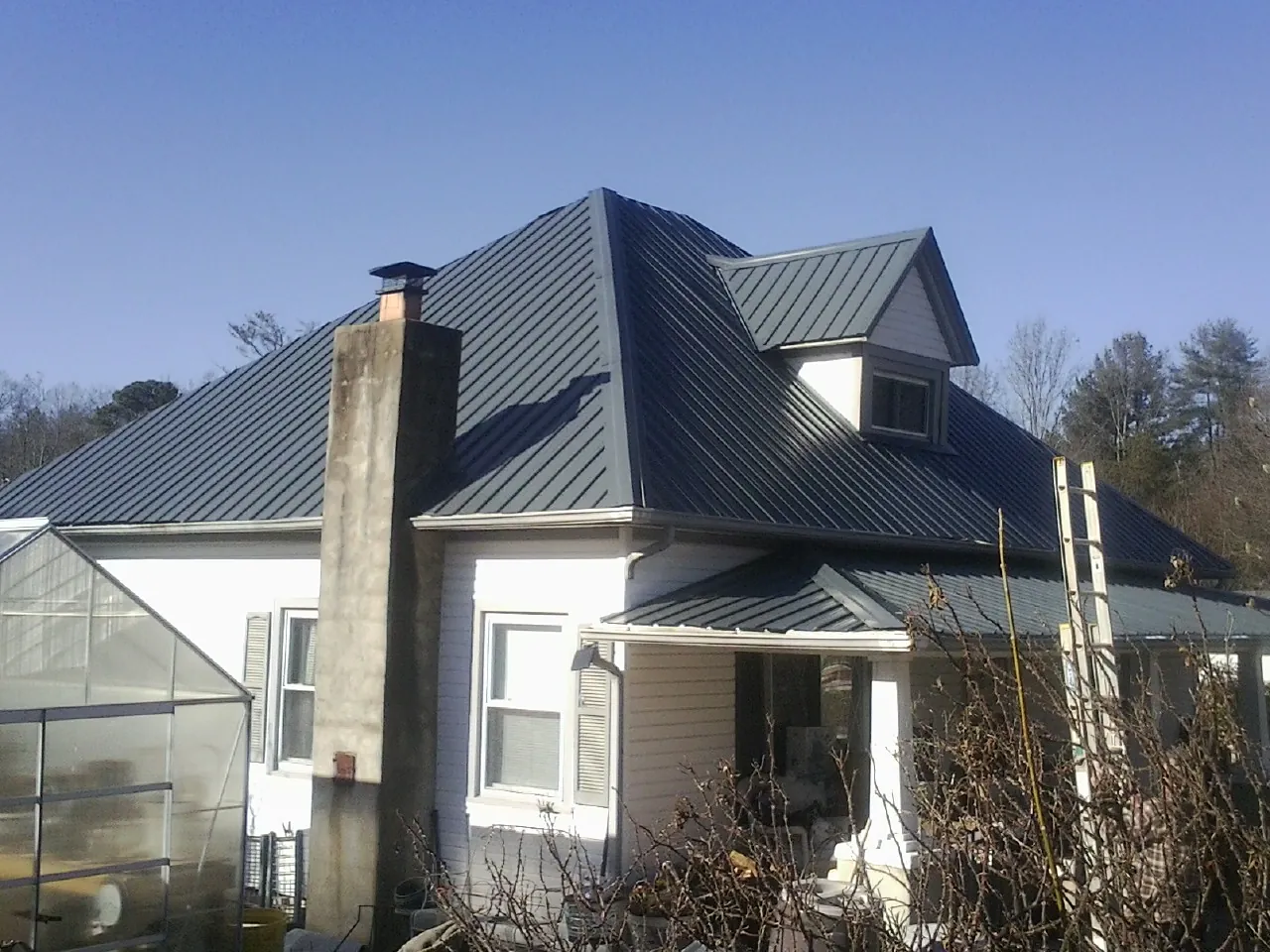 Dark blue standing seam metal roof on a white farmhouse with dormer — Slate & Tile Roof Repair by Roofing Brothers in Doerun