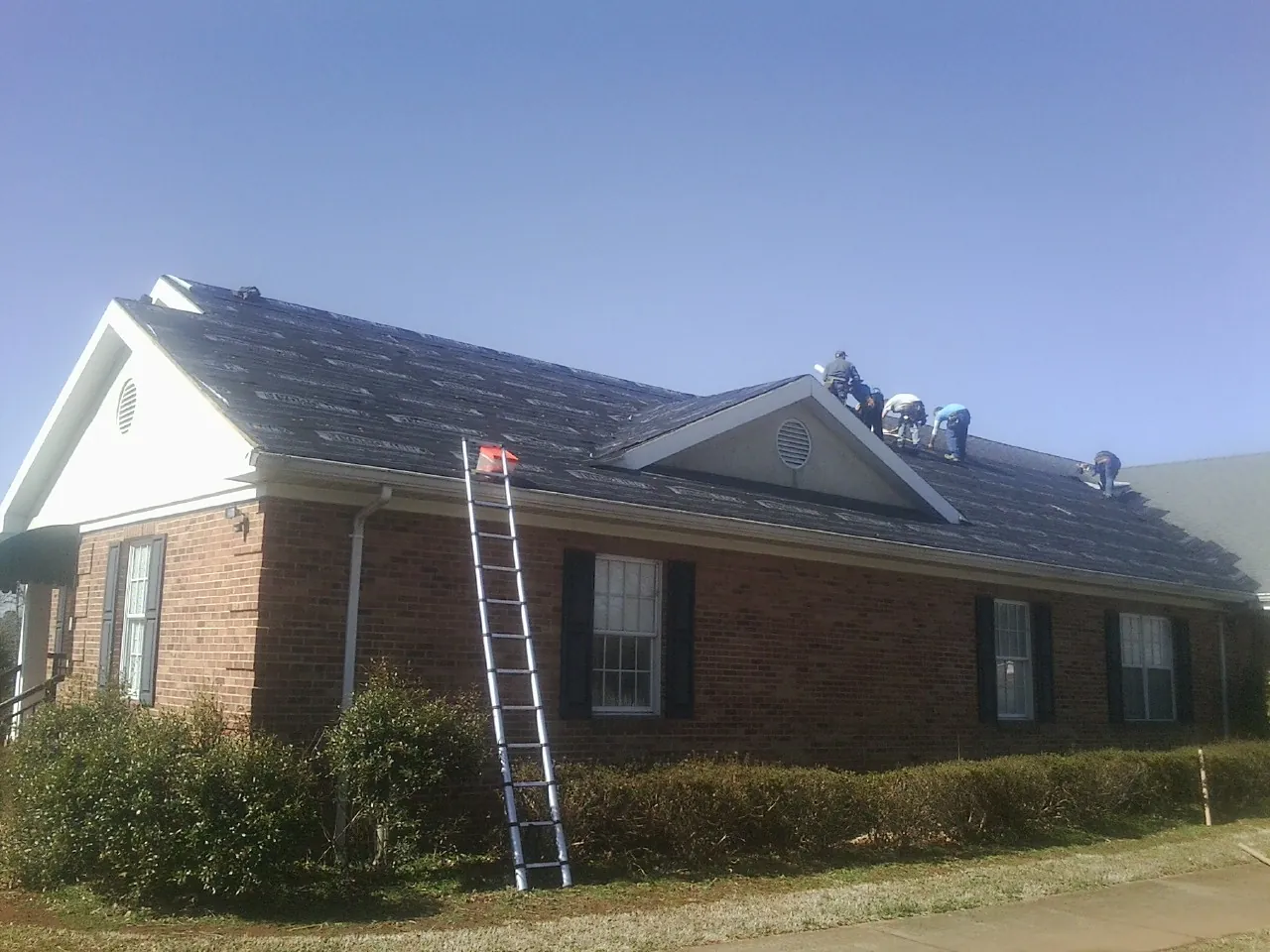 Crew tearing shingles off a brick ranch roof with a ladder set — Emergency Roof Repair work by our crew in Doerun