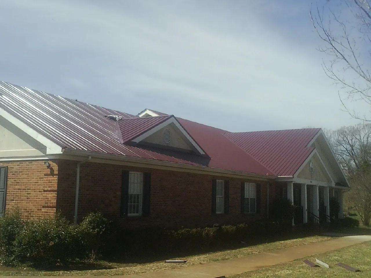 Red metal roof with gabled entries on a long brick building, from a Hail Damage Roof Repair job in Doerun