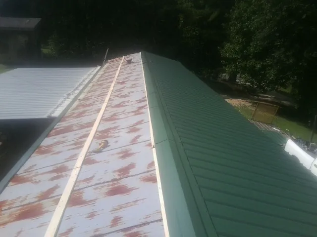 Old rusted panels beside newly installed green metal roofing — Wind Damage Roof Repair by Roofing Brothers in Doerun