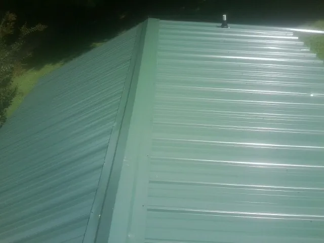 New green metal panels meeting at the ridge of a roof — Flat Roof Repair work by our crew in Doerun