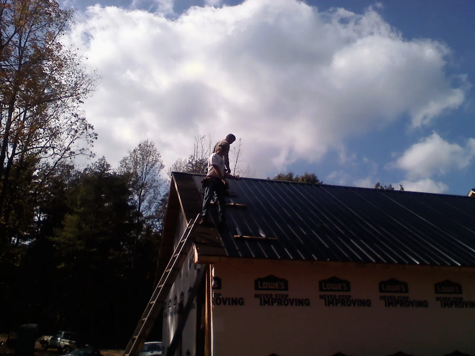 Roofer fastening dark metal panels high against a cloudy sky, from a Roof Inspection job in Doerun