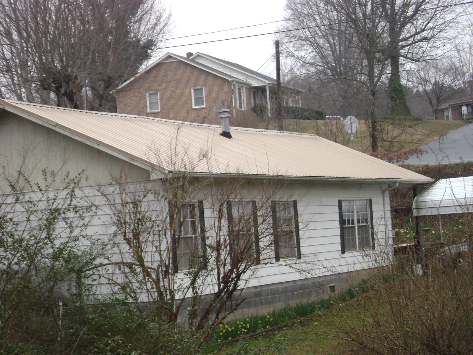 Tan metal roof on a white sided house set into a hillside — Commercial Roofing by Roofing Brothers in Doerun