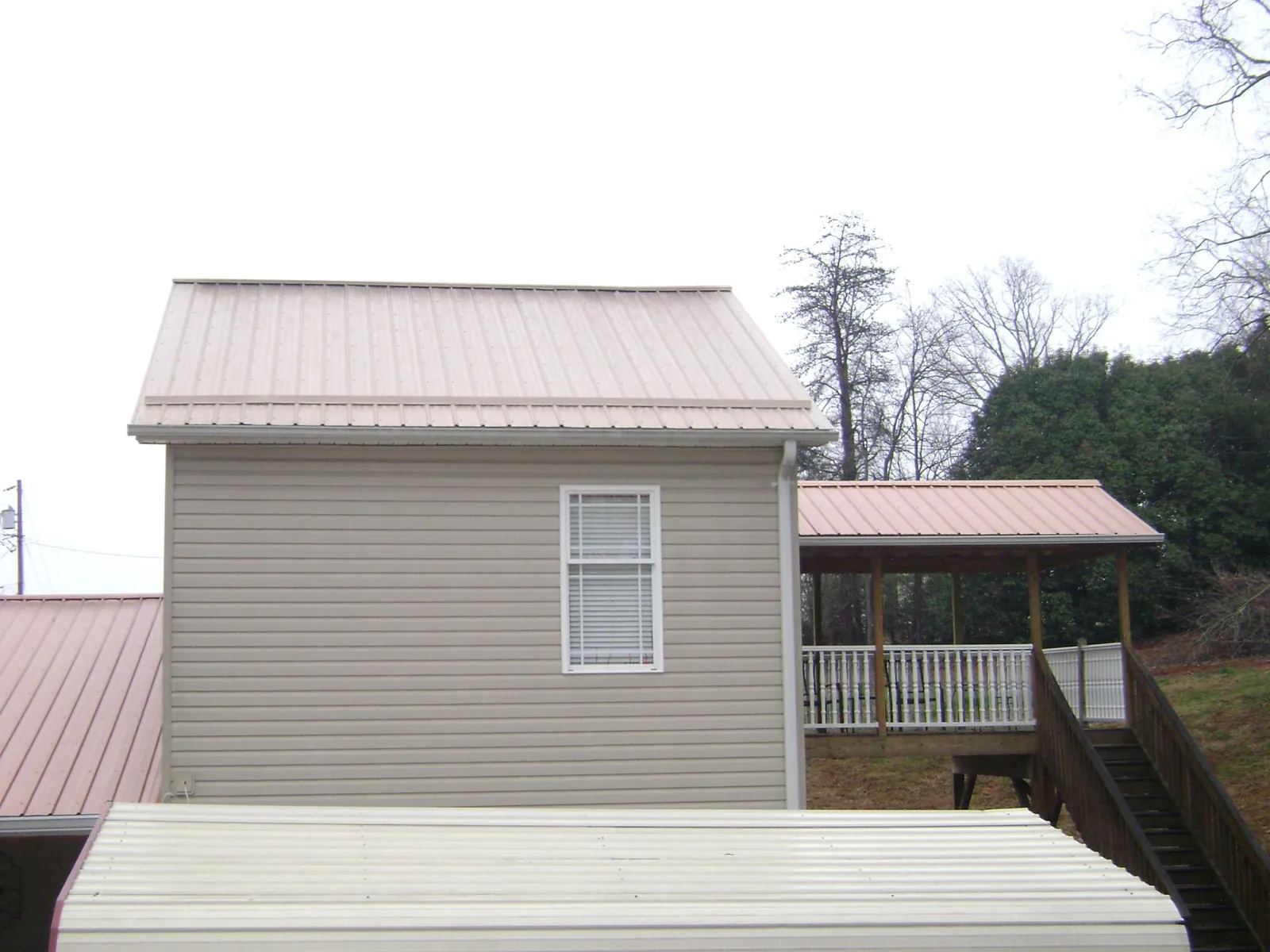 Tan metal roofs on a two story addition and attached porch, from a Roof Replacement job in Doerun